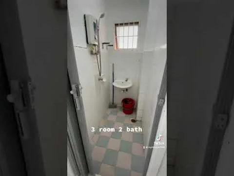 Bathroom features: shower with handheld showerhead, white sink, white tiled walls, checkered floor tiles in blue and white, window with grid pattern, toilet, mirror, red bucket.