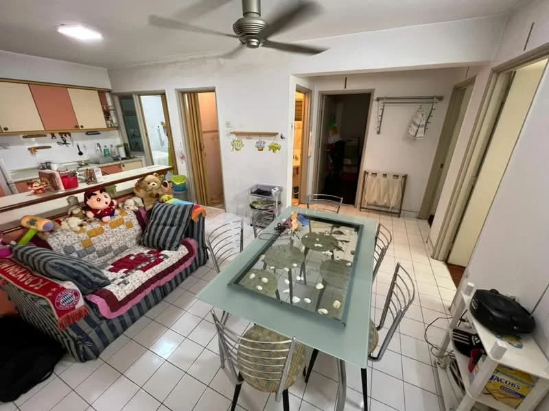 Living features: 3-seater fabric sofa with colorful throw pillows, glass dining table with metal legs, 6 dining chairs, ceiling fan, white painted walls, tile flooring, open kitchen area, decorative wall art, stuffed toys on sofa, built-in cabinets in kitchen, refrigerator visible in background, laundry area with drying rack; style: modern.