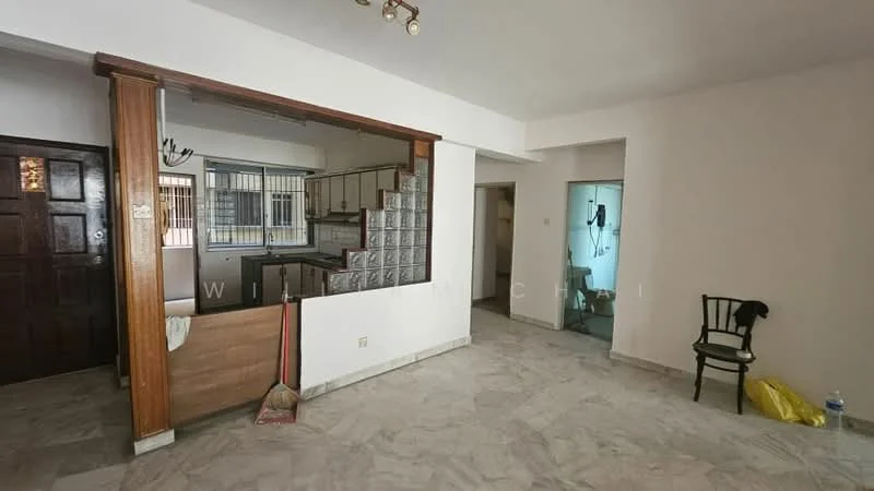 Living features: marble flooring, white painted walls, wooden door, glass block partition, ceiling lights, open layout to kitchen, window with grille, broom and dustpan on floor, chair in corner, water bottle on floor. Kitchen features: white cabinetry, countertop with sink, open layout to living room, window with grille. Room features: doorway leading to another room, light-colored walls.