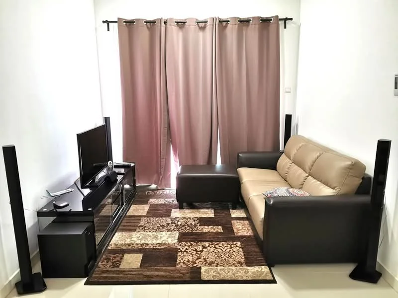 Living features: beige leather sofa, black coffee table, black TV console, wall-mounted TV, area rug with geometric pattern, two black floor speakers, light grey walls, cream tiled flooring, curtains in light brown, decorative cushion on sofa; style: modern.