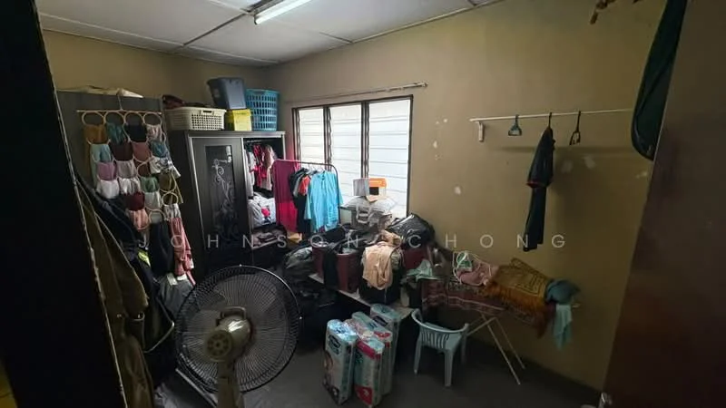 Laundry features: grey tiled flooring, cream painted walls, window with white frame, clothes drying rack, plastic laundry basket, clothes hanging on wall-mounted hooks, black wardrobe, stack of toilet paper rolls, standing fan.