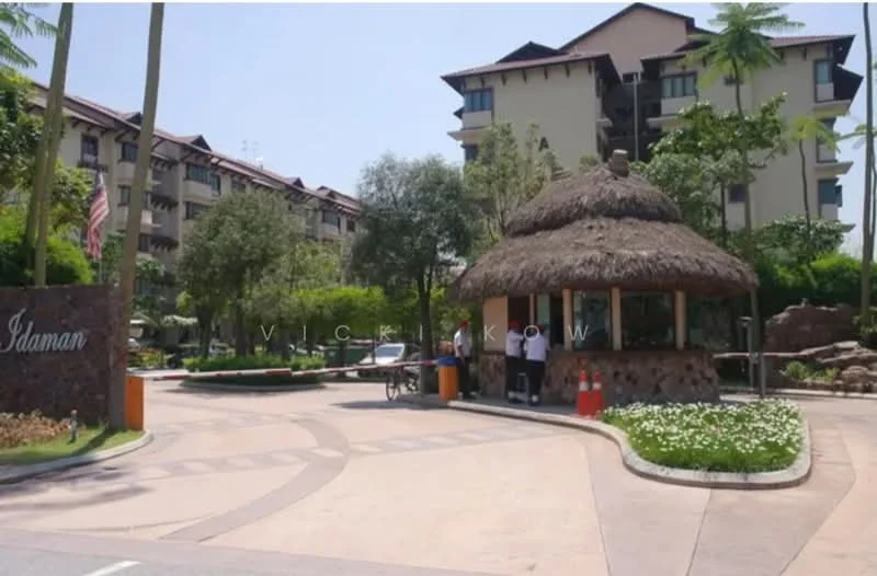 Exterior type: low-rise apartment block; features: thatched roof guard house, landscaped garden with flowering plants, paved driveway, mature trees, stone cladding on guard house, signage at entrance, surrounding greenery, multiple storeys visible, parking area; style: tropical-modern.