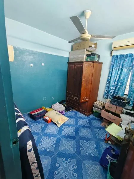 Room features: blue painted walls, ceiling fan, wooden wardrobe, blue patterned tile flooring, curtains with floral pattern, boxes stacked on top of wardrobe, various storage boxes on the floor, air conditioning unit.