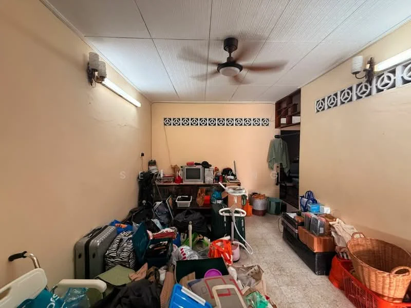 Room features: light beige painted walls, ceiling fan, tile flooring, multiple storage boxes, suitcases, various bags, microwave, clothes hanging on a rack, baskets, cluttered layout, wall-mounted light fixtures.