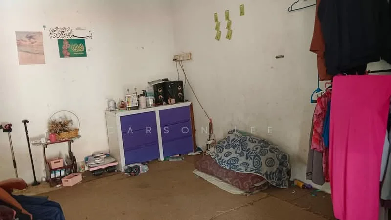 Room features: white painted walls, carpet flooring, small bedside table, purple storage cabinet, clothes hanging on wall, floor cushions, decorative wall art, small fan, various personal items on shelves.