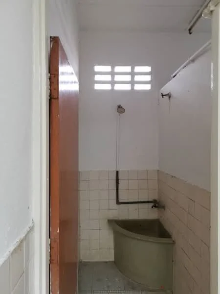Bathroom features: white tiled walls, grey tiled flooring, bathtub, shower head, wall-mounted faucet, window with ventilation bars, pipe fittings, white painted ceiling.