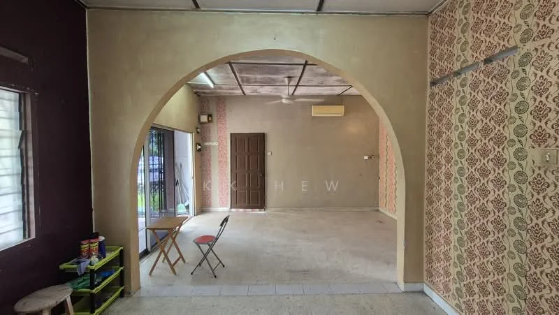 Room features: arched doorway, plain ceiling, wall with floral wallpaper, plain painted walls, tile flooring, window with security bars, air conditioning unit, wooden door, small folding table, single chair, open floor space; style: traditional.