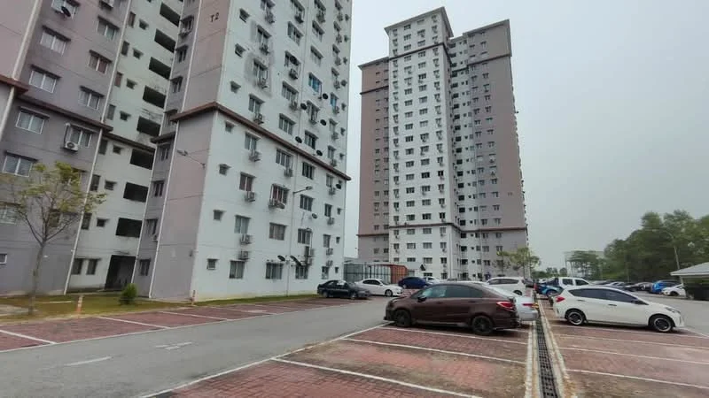 Exterior type: mid-rise condominium; features: grey painted facade, balconies on upper floors, multiple storeys, parking lot with marked spaces, landscaped area with small trees, surrounding greenery, driveway with interlocking pavers; style: modern.