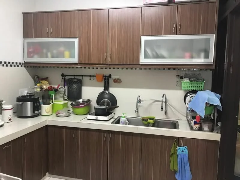 Kitchen features: brown wooden cabinetry, white countertop, double-bowl stainless-steel sink, chrome pull-down faucet, stainless-steel gas hob, microwave, rice cooker, various cooking utensils, green plastic storage basket, wall-mounted pot rack, decorative wall tiles with black border; style: modern.