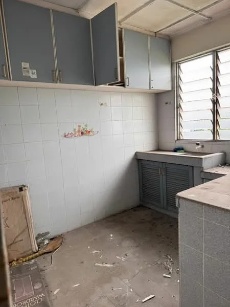 Kitchen features: grey cabinetry with upper and lower storage, white tiled walls, grey countertop, single-bowl sink, window with horizontal slats, unfinished flooring, exposed wall with decorative painting, visible debris on the floor.