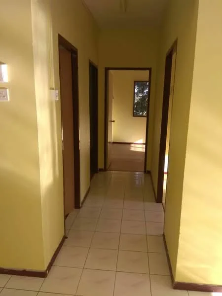 Hallway features: yellow painted walls, ceramic tile flooring, wooden doors, door frames, natural light from windows, light fixture on ceiling.
