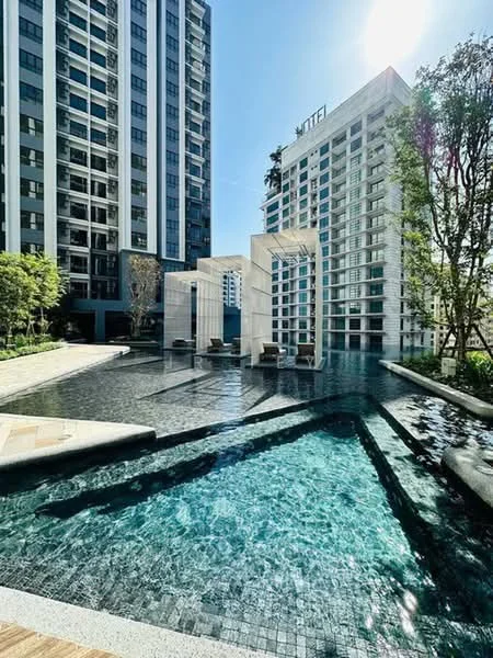 Exterior type: high-rise condominium; features: infinity pool, pool deck with loungers, landscaped garden, water feature, surrounded by greenery, modern architecture, glass facade, stone-paved walkway; style: modern.