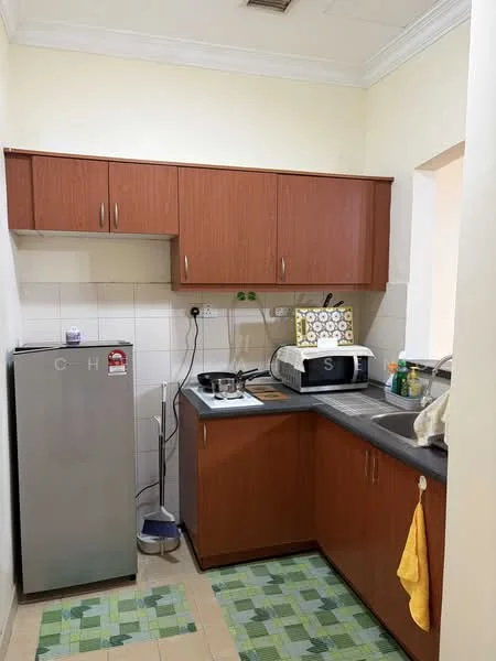 Kitchen features: brown wooden cabinetry, grey countertop, stainless-steel fridge, double-bowl stainless-steel sink, chrome faucet, gas stove with two burners, microwave, kitchen towel, green and beige tiled flooring, wall tiles, power outlet, decorative wall clock.