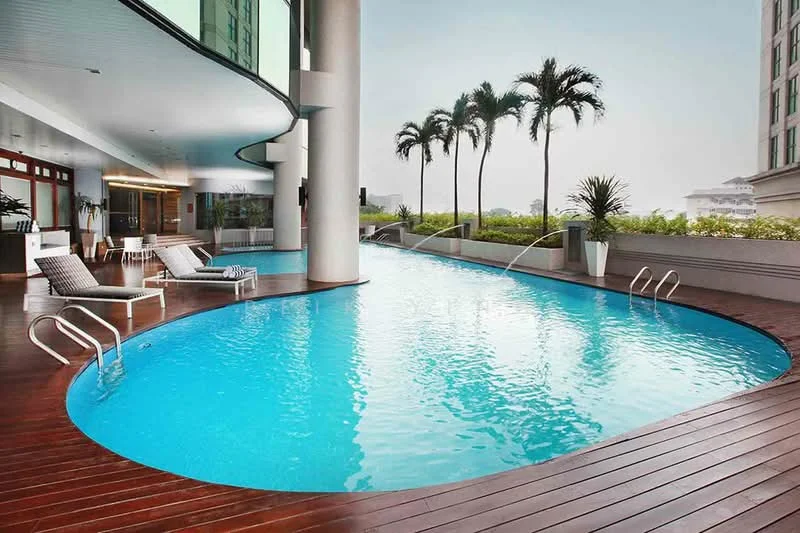 Exterior type: swimming pool deck; features: infinity pool, wooden deck flooring, lounge chairs, palm trees, landscaped garden, glass railing, poolside loungers, modern architecture, outdoor seating area; style: modern.