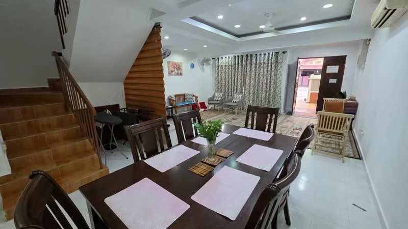 Dining features: dining table with 6 chairs, white placemats on table, wooden dining chairs, ceiling fan, recessed downlights, white painted walls, tile flooring, area rug with geometric pattern, decorative wall art, curtains with floral pattern, staircase with wooden steps, open layout to living area; style: modern. Living features: sofa seating area, coffee table, TV console, area rug, wooden flooring, wall-mounted air conditioning unit; style: modern.
