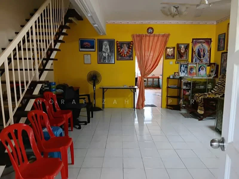 Living features: white tiled flooring, yellow painted walls, wooden staircase, ceiling fan, wall-mounted artwork, framed photographs, table with chairs, red plastic chairs, standing fan.