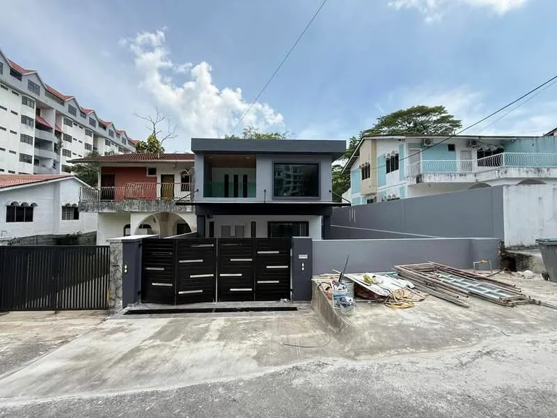 Exterior type: detached bungalow; features: grey painted facade, flat roof, two-storey structure, black metal gate, concrete driveway, manicured lawn, surrounded by residential buildings, visible construction materials on the ground; style: modern.