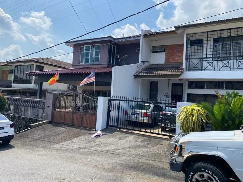 Exterior type: semi-detached house; features: white painted facade, red brick accents, flat roof, double-storey, manicured lawn, paved driveway, metal gate, visible car parked in driveway, flagpole with flags, surrounded by greenery; style: modern.
