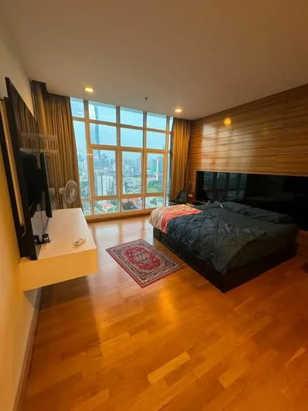 Bedroom features: king-size bed with dark bedding, wooden flooring, floor-to-ceiling windows, city skyline view, wall-mounted TV, white console table, decorative area rug, curtains, ceiling lights, wood panel accent wall, fan; style: modern; view: city.