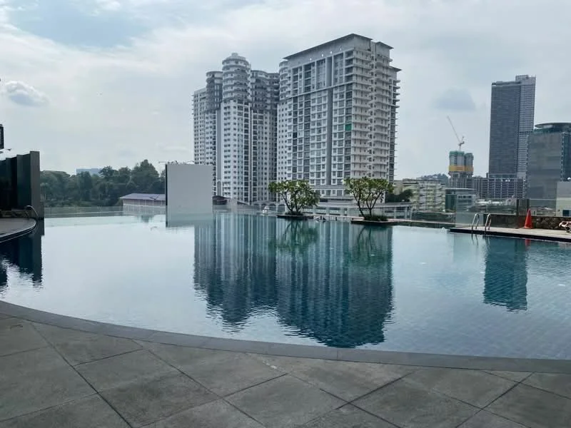 Exterior type: high-rise condominium; features: infinity pool, pool deck with loungers, surrounded by mature greenery, city skyline in background, modern architectural design, glass curtain wall, manicured landscaping; style: modern.