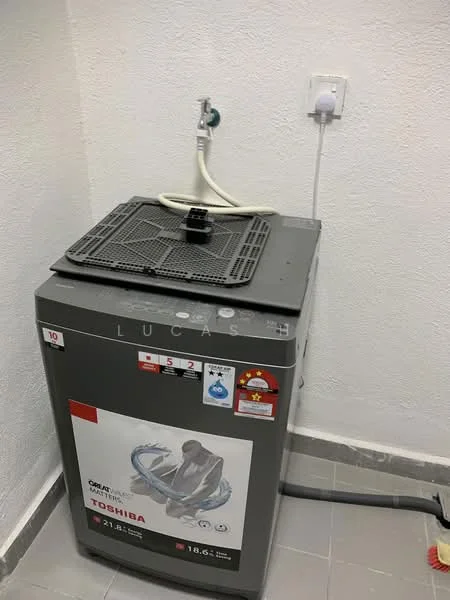 Laundry features: top-loading washing machine, grey exterior, water inlet hose, drain hose, power outlet, tile flooring, white painted walls.