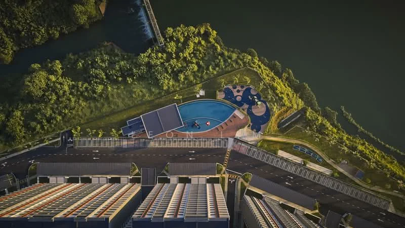 Exterior type: high-rise condominium; features: infinity pool, pool deck with loungers, landscaped garden, surrounded by greenery, waterfront view, multi-storey car park, access road, adjacent to water body; style: modern.