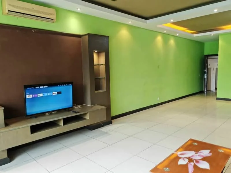Living features: green painted walls, brown accent wall, white tiled flooring, ceiling with recessed lighting, wall-mounted TV, built-in shelving unit, 1 wall-mounted split AC, light fixtures, doorway leading to another room; style: modern.