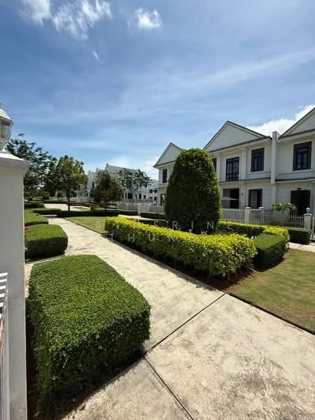 Exterior type: linked terrace house; features: manicured lawn, hedge landscaping, paved walkway, two-storey houses, white painted facade, gated community, mature trees, clear blue sky; style: modern.
