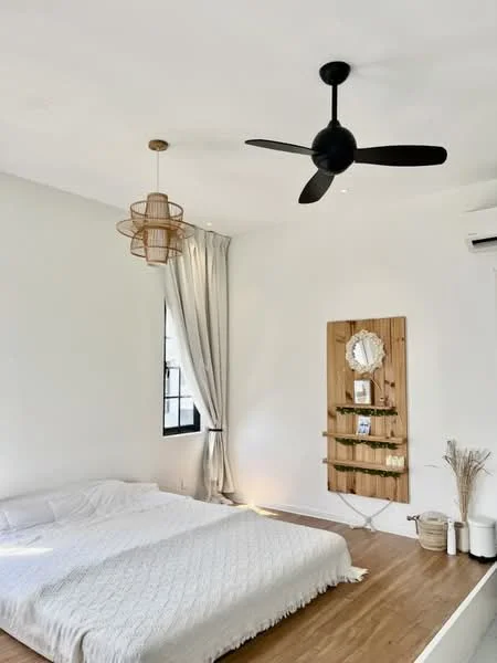 Bedroom features: king-size bed with white bedding, wooden flooring, black ceiling fan with 5 blades, hanging rattan light fixture, white painted walls, floor-to-ceiling window with sheer curtains, wooden wall-mounted shelf, decorative mirror, decorative plants in ceramic pots; style: minimalist.