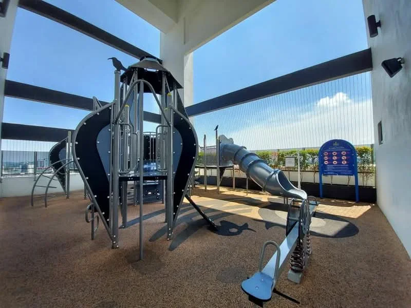 Exterior type: playground; features: play structure with climbing frame, slide, safety flooring, open-air design, surrounding safety netting, urban skyline view, sunlight exposure, playground equipment for children; style: modern.