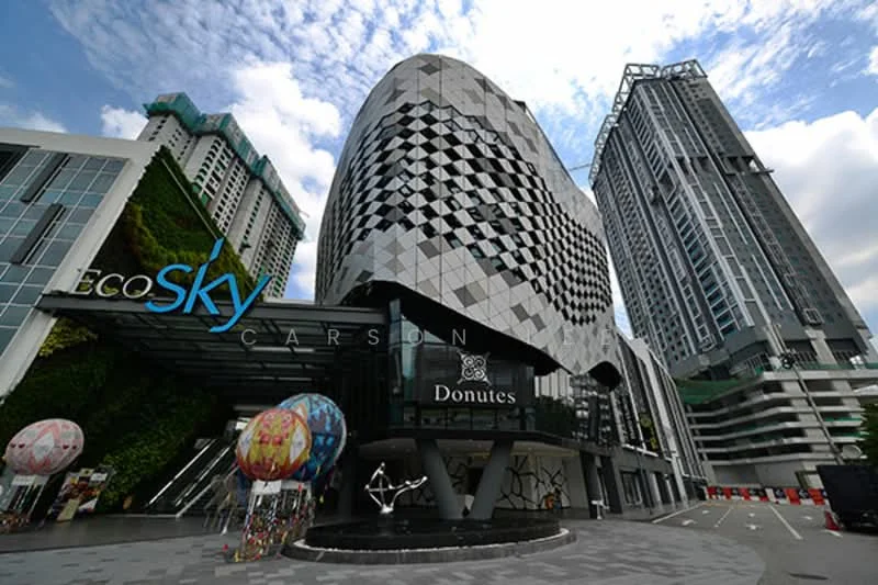 Exterior type: high-rise condominium; features: modern facade with geometric patterns, glass curtain wall, prominent entrance with artistic sculpture, decorative balloons at entrance, surrounding high-rise buildings, greenery on building facade; style: contemporary.
