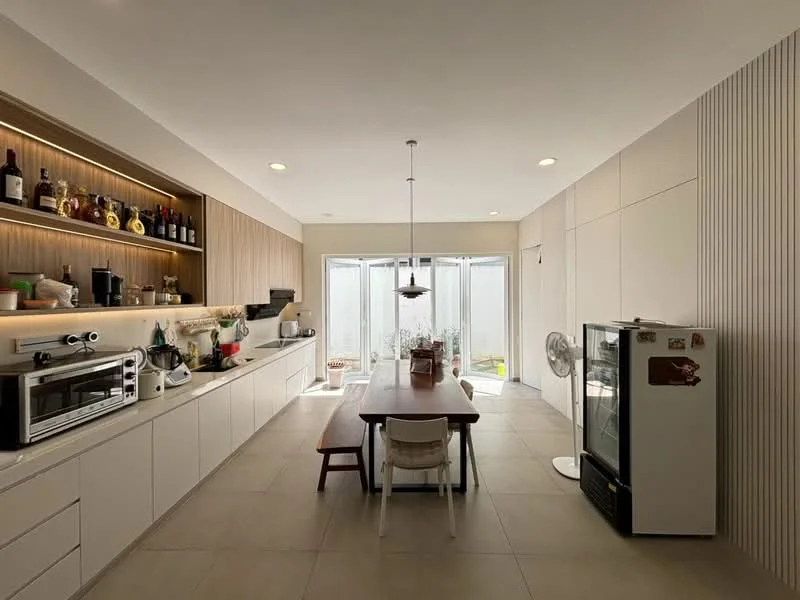 Kitchen features: white cabinetry with flat-panel design, wooden countertop, stainless-steel refrigerator, built-in oven, microwave, kitchen island with seating, pendant light above dining table, 5-blade ceiling fan, ceramic tile flooring, wall-mounted shelving with glassware, floor-to-ceiling windows, sliding glass door, decorative plants on countertop; style: modern; view: garden.