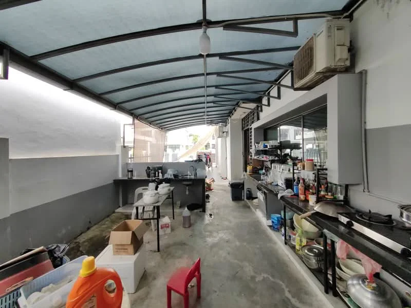 Room features: concrete flooring, grey painted walls, metal roof with blue panels, overhead lighting, open layout, kitchen counter with storage, multiple shelves with kitchenware, stainless-steel sink, gas stove, air conditioning unit, plastic chairs, boxes and containers.