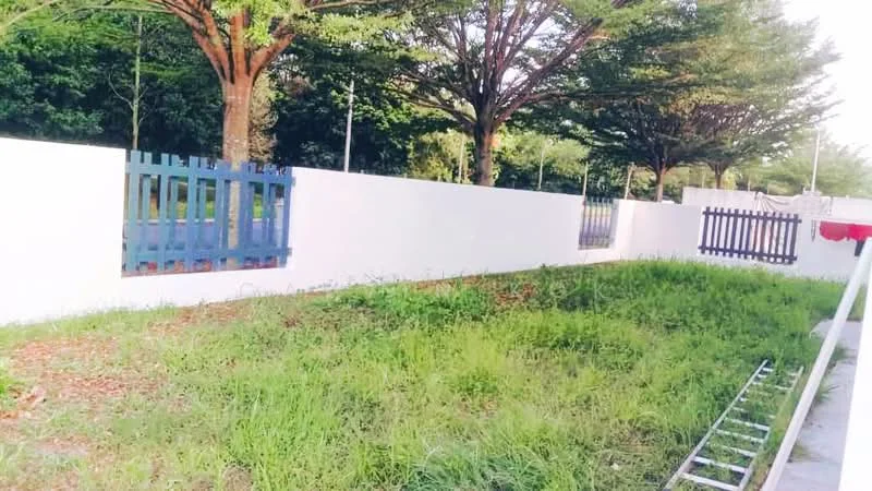 Exterior type: landscape garden; features: white painted wall, green grass area, mature trees, wooden fence with blue paint, wooden fence with dark brown paint, ladders visible, paved walkway; style: modern.