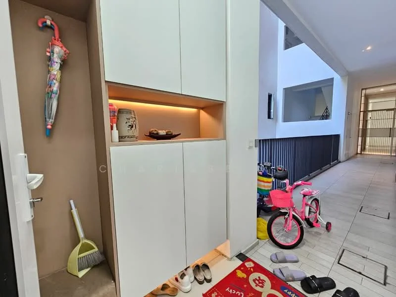 Room features: built-in storage cabinet with white finish, decorative wall art, floor tiles in light color, shoe mat at entrance, cleaning supplies visible, children's bicycle, slippers on the floor, natural light from adjacent space; style: modern.