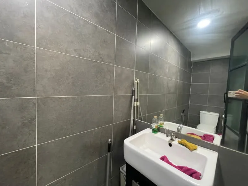 Bathroom features: grey tile cladding on walls, white ceramic sink, chrome basin mixer faucet, one-piece toilet, mirror, recessed lighting, towel rack, hand towel, bottle of water, cleaning supplies; style: modern.