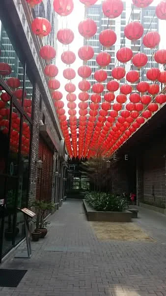 Exterior features: red lanterns hanging from above, brick facade, paved walkway, landscaped planters, greenery along the pathway, modern high-rise buildings in background; style: modern.