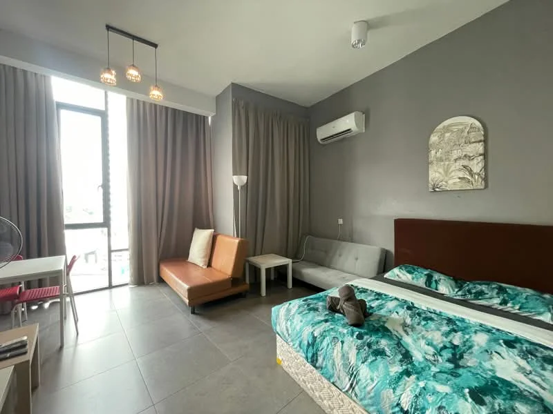Room features: grey painted walls, tile flooring, queen-size bed with patterned bedding, sofa in brown leather, 2-seater fabric sofa in light grey, white coffee table, floor lamp, wall-mounted air conditioning unit, large window with sheer curtains, ceiling light fixture with multiple bulbs, dining table with red chairs; style: modern.