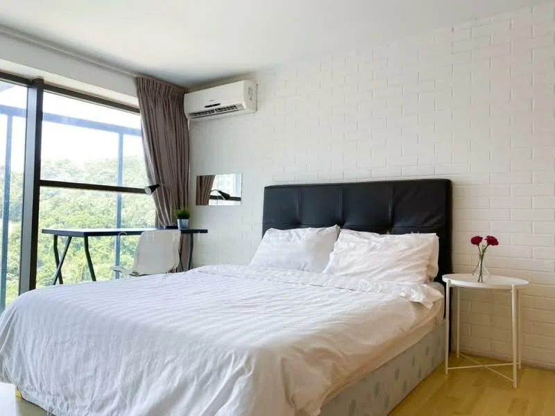Bedroom features: king-size bed with white bedding, black upholstered headboard, wooden flooring, floor-to-ceiling windows, curtains, wall-mounted air conditioning unit, white brick accent wall, small round side table, decorative vase with flowers, small desk or table, green plant, natural light from windows; style: modern; view: garden.