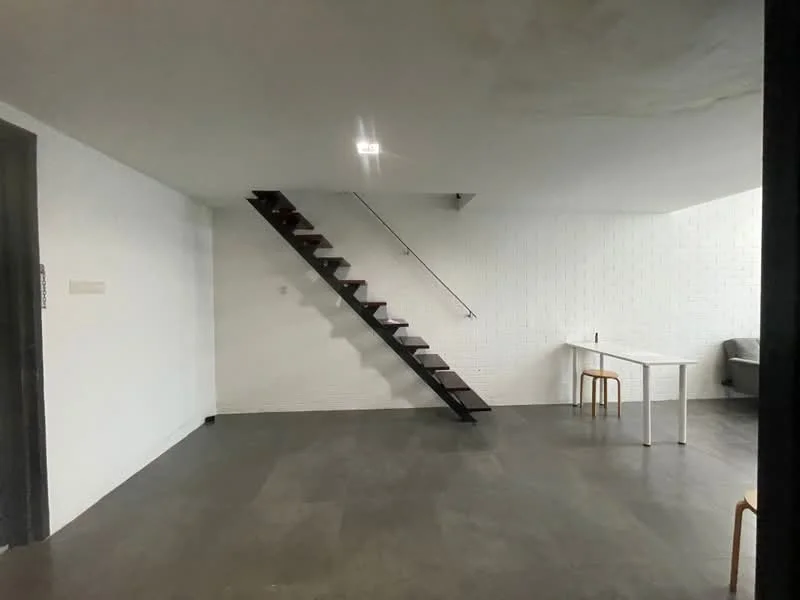 Room features: white painted walls, exposed brick wall, dark wood staircase, grey tile flooring, recessed downlights, white table, two wooden chairs, open space layout; style: modern.