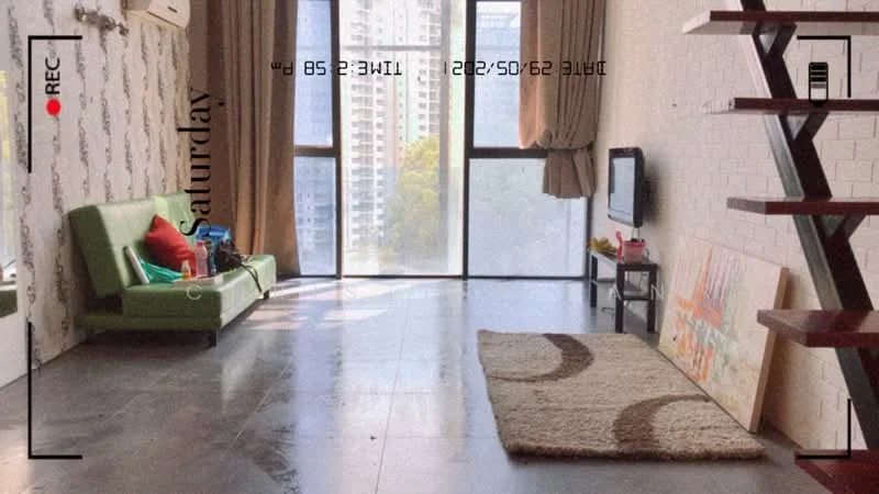 Living features: green fabric sofa, coffee table, wall-mounted TV, floor-to-ceiling windows, curtains, area rug with circular pattern, exposed brick wall, grey tile flooring, air conditioning unit, staircase with wooden steps; style: modern; view: city.