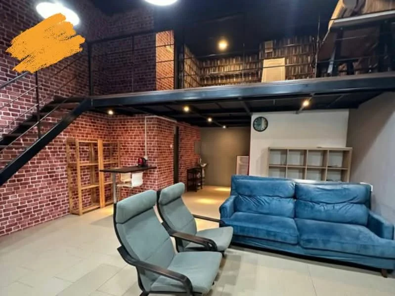 Living features: exposed brick walls, grey tiled flooring, metal staircase, sofa in blue fabric, two armchairs in grey fabric, recessed downlights, wall-mounted clock, open shelving unit, wooden dining table, bookshelves on upper level; style: industrial.