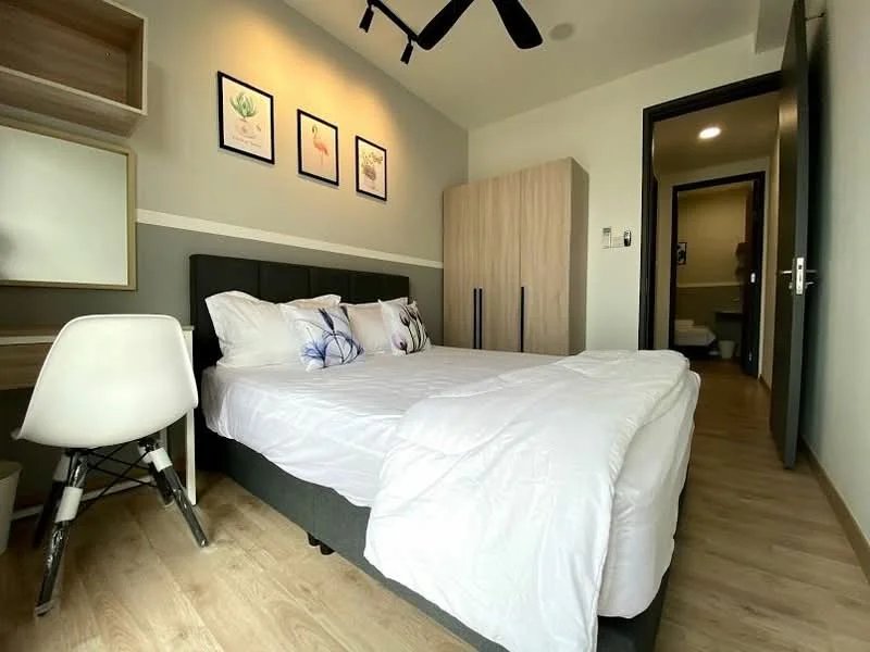 Bedroom features: queen-size bed with white bedding, upholstered headboard, 2 bedside pillows with floral design, wooden flooring, ceiling fan, wall-mounted artwork with botanical prints, built-in wardrobe with wood finish, study desk with white chair, mirror on wall, light switch on wall; style: modern.