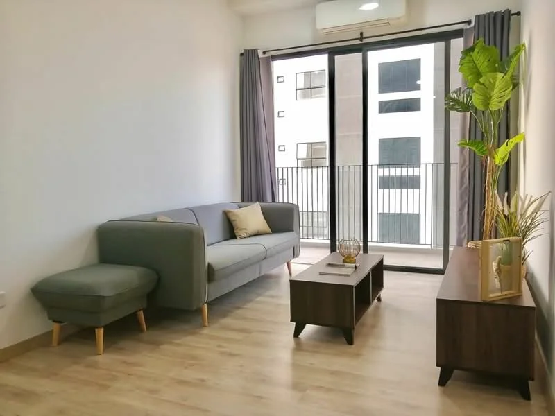 Living features: grey fabric sofa, ottoman, wooden coffee table, TV console, floor-to-ceiling windows, curtains, wooden flooring, indoor plant, decorative vase, wall-mounted air conditioning unit; style: modern; view: city.