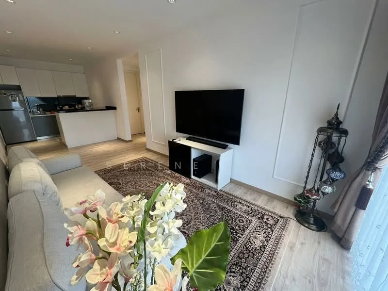 Living features: light grey fabric sofa, white TV console, wall-mounted flat-screen TV, decorative rug with intricate pattern, wooden flooring, recessed ceiling lights, floor-to-ceiling windows with sheer curtains, indoor plants in ceramic pots; style: modern. Kitchen features: stainless-steel fridge, white cabinetry, black countertop, open layout to living area; style: modern.