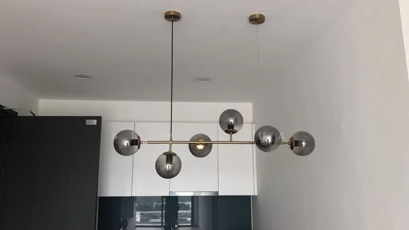 Kitchen features: modern pendant light with multiple spherical bulbs, white cabinetry, black countertop, stainless-steel appliances, open layout, recessed ceiling lights, smooth wall finish, floor-to-ceiling windows; style: modern.