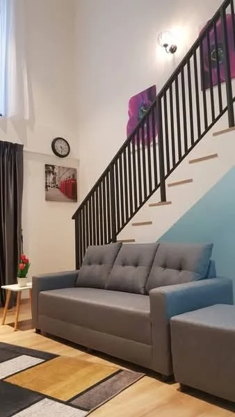 Living features: grey fabric 3-seater sofa, light wood side table, black metal railing, staircase with wooden steps, wall-mounted light fixture, decorative wall art with flowers, clock on the wall, curtains in dark grey, area rug with geometric pattern, laminate flooring; style: modern.
