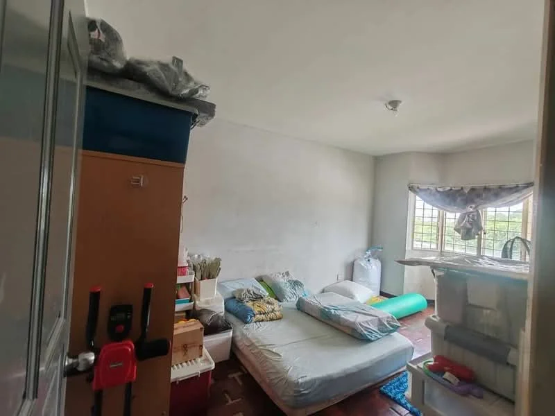 Bedroom features: single bed with mattress, pillow and bedding, wooden flooring, window with grid bars, curtains, wall-mounted light fixture, cluttered storage with boxes, green exercise mat, white walls, ceiling light, door leading to hallway.