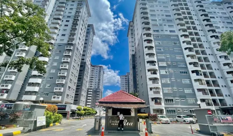 Exterior type: high-rise condominium; features: grey painted facade, multiple storeys, gated entrance, guard house at entrance, landscaped greenery, parking spaces visible, surrounded by mature trees, clear blue sky; style: modern.