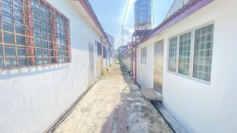 Exterior type: linked terrace house; features: white painted facade, narrow pathway, water tank on roof, single-storey, windows with metal grilles, concrete walkway, surrounding residential buildings; style: modern.